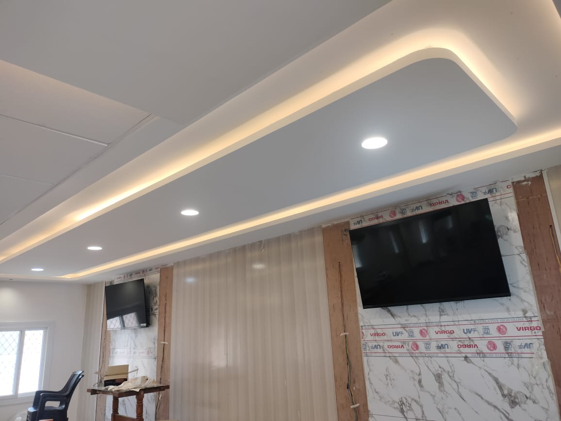 Curved gypsum false ceiling with concealed cove lighting above a living room TV unit